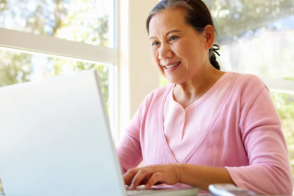 An older woman using a laptop with a smile.