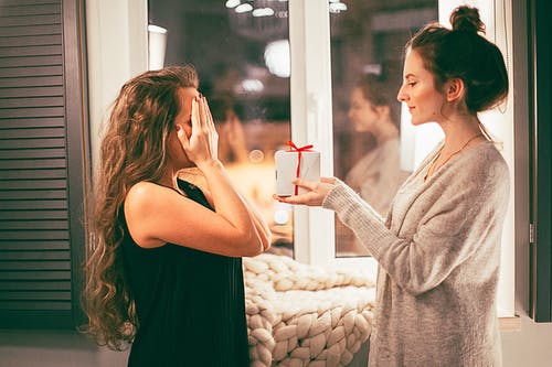 A woman surprising her friend with a gift in a box.