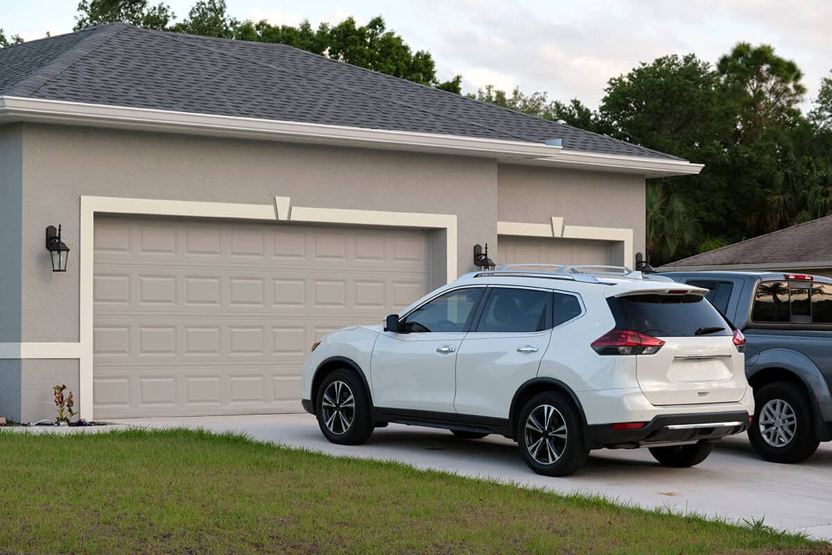 White SUV parked in a driveway outside of a house in front of the garage.