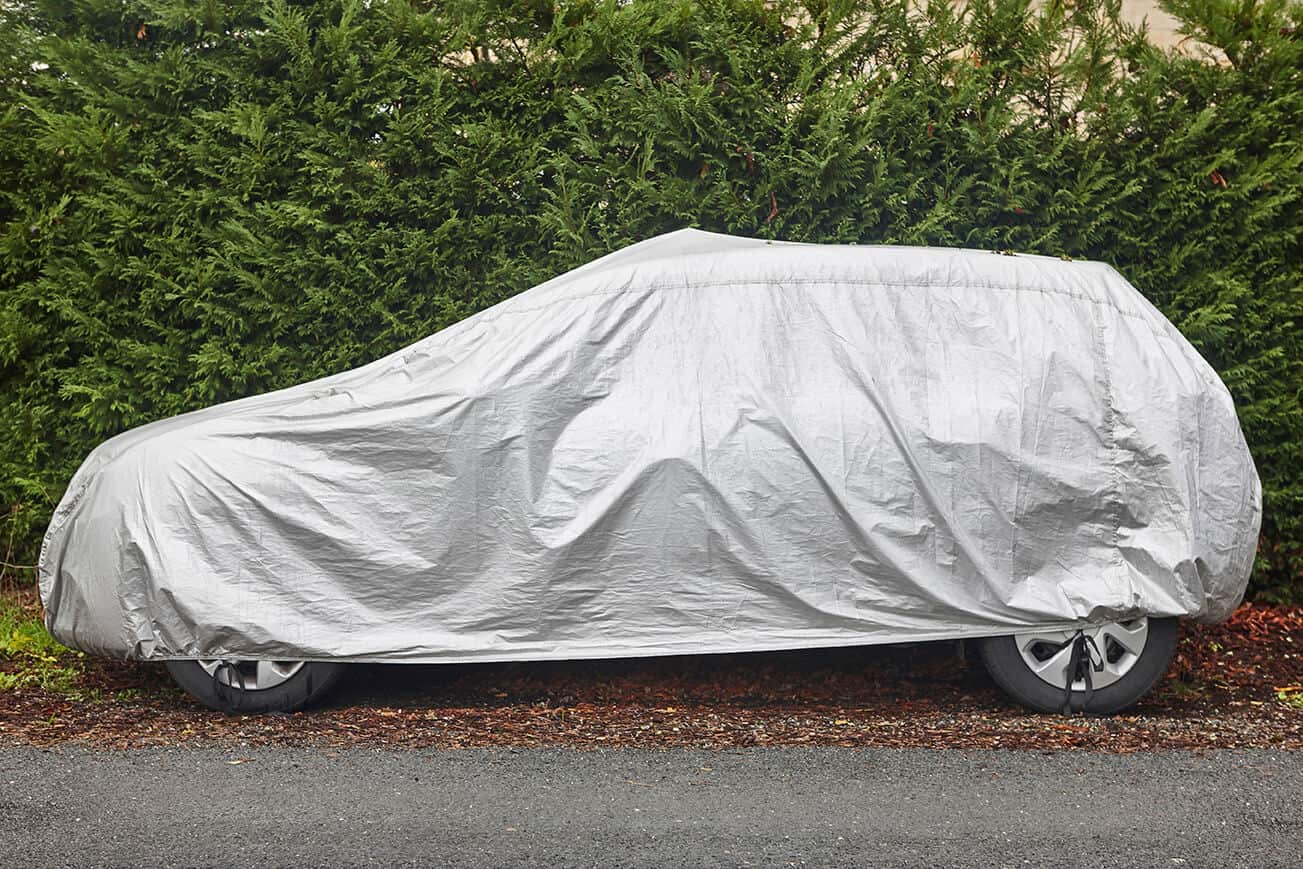 SUV parked on the side of a driveway with a grey car cover over it.